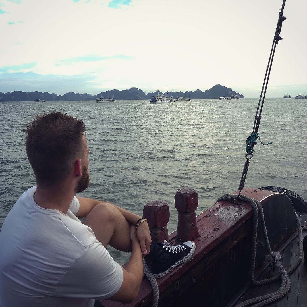 Arnaud Bruckler assis à l'avant d'un bateau, les îles calcaires de la baie d'Ha Long à l'horizon